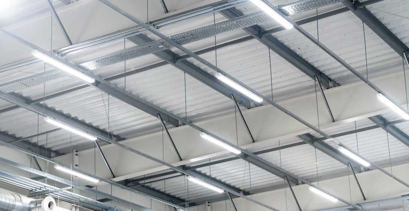 LED Beleuchtung im Lager von Steidinger Decke eines Gebäudes aus Stahl und Aluminium mit sichtbaren Trägern und Leuchtstofflampen.